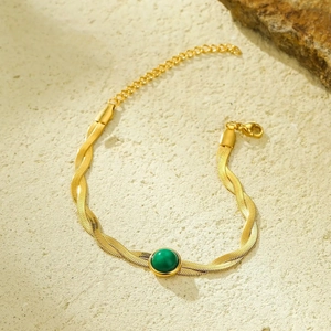 Close-up of golden braided snake chain bracelet with green gemstone and lobster clasp