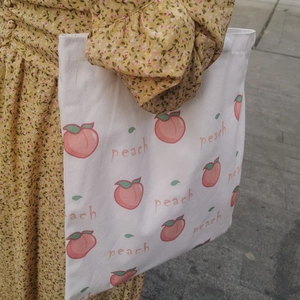 Close-up of a white canvas tote bag with pink peach prints held against a floral dress