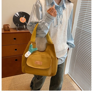 Detail of yellow canvas tote bag with leather logo and cute plush character pendant