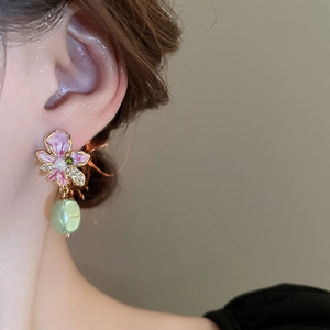 Detailed view of pink enamel flower earrings with a green pearl drop on a female model