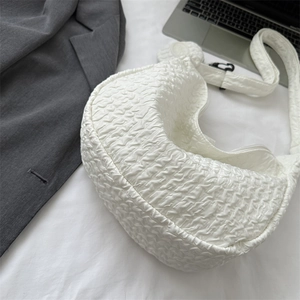 Minimalist white puffy cloud shoulder bag with textured fabric next to laptop