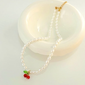 Elegant pearl necklace with red cherry pendant and gold chain on white ceramic
