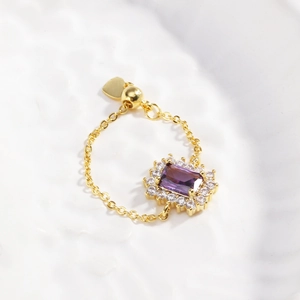 Detailed macro of gold chain ring featuring a purple stone and adjustable heart charm
