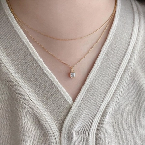 Detail of layered gold link necklace featuring a square clear crystal pendant on model