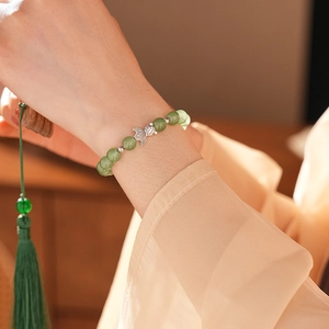 Close-up of green jade chalcedony bead bracelet with silver fish charm on model wrist