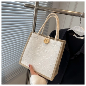 Close-up of beige linen tote bag with white lace floral embroidery and a large wooden button