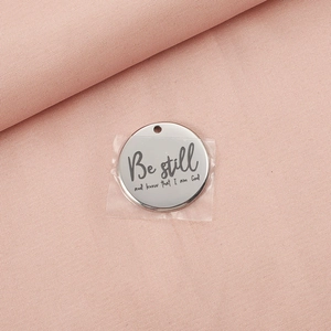 Macro shot of silver metal round charm engraved with Be still and know that I am God