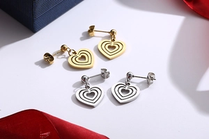 Detail view of multi-layer heart drop earrings in gold and silver steel on a white surface