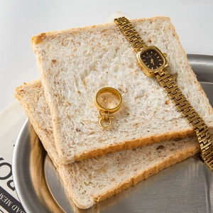 Close-up of a gold square watch and ring displayed on bread slices for a luxury look
