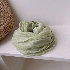 Detail of light green pleated scarf with natural texture next to a woven straw bag