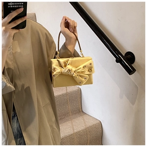 Detail of gold satin evening bag with crystal bow and metallic chain strap in bright light
