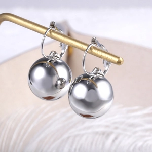 Close-up of polished silver sphere drop earrings hanging on a luxury display stand