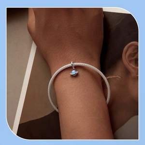 Close-up of a silver mesh bracelet featuring a blue starry planet charm on a wrist