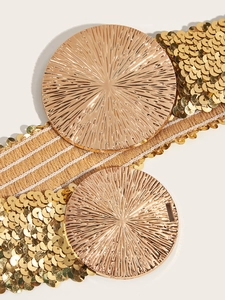 Detail of a wide gold sequined elastic waist belt featuring a large round textured buckle