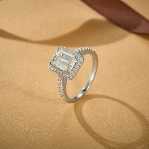 Macro view of emerald-cut moissanite ring with halo setting on champagne background