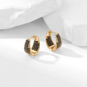 Detail of gold geometric hoop earrings with pavé black zircons on a white stone base