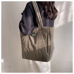 Close-up of olive green quilted nylon tote bag with brand plaque worn by a model