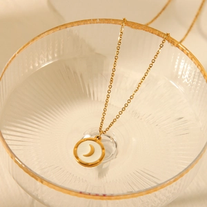 Close-up of gold moon necklace with white enamel inlay resting in a glass bowl