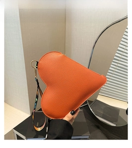 Détail d'une pochette orange en forme de cœur, texture litchi et dragonne brodée LOVE