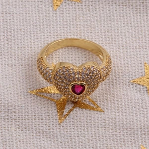 Gros plan détaillé d'une bague cœur dorée avec pierre rouge et pavage de zircons blancs