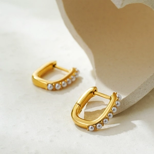 Detail of 18K gold rectangular hoop earrings with small grey pearls on textured surface