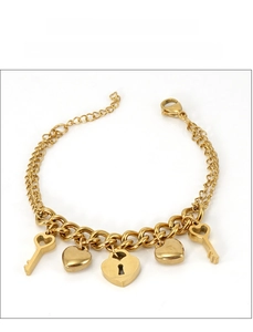 Détail des breloques cœur et clé dorées 18K sur un bracelet gourmette en acier inoxydable