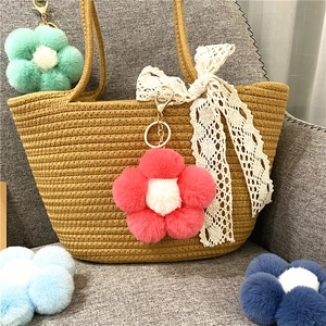 Detail view of colorful plush flower keychains hanging on a straw tote bag charm