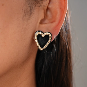 Close-up of vintage heart stud earring with golden hammer texture and black enamel
