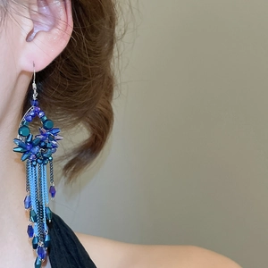 Detailed side view of long tassel earrings with blue crystals and silver chains on model