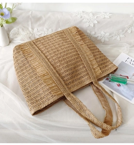 Detail of a large khaki straw woven tote bag with fringe accents for a vacation style