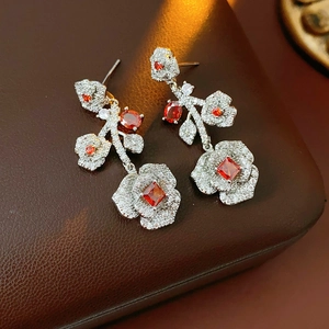Detail view of vintage silver rose earrings with red and clear zircon on brown leather