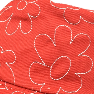 Détail de la broderie florale blanche sur chapeau en coton rouge avec texture de sergé
