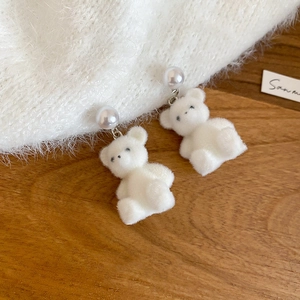 Detail of white flocked bear earrings with a pearl stud on a rustic wooden background