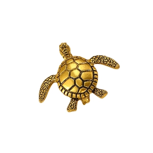 Détail d'une broche tortue dorée avec motifs géométriques de carapace sur fond blanc