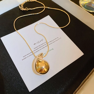 Macro view of a glossy gold teardrop pendant on a fine snake chain necklace