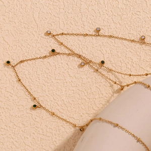 Detail of 18K gold-plated necklace with green and clear zircon beads on textured surface