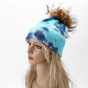 Detail of blue tie-dye knit beanie featuring a large fluffy brown pom-pom on top