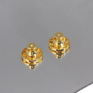 Detail showing two gold disc earring lifters with ornate cut-outs on a reflective surface