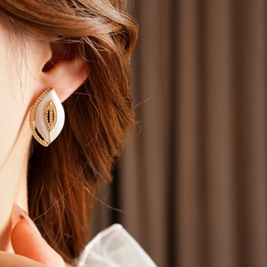Nahaufnahme von Vintage-Ohrringen mit Goldrand und weißer Emaille in Blattform