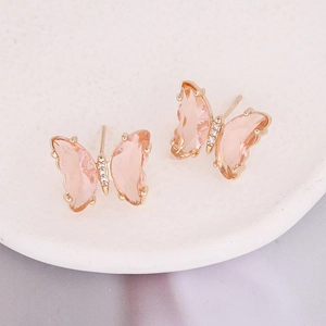 Macro view of butterfly earrings with peach zircon stones on a white ceramic plate