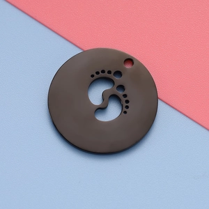Detailed close-up of a black metal round pendant with a cutout baby footprint design