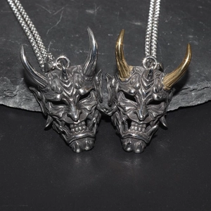 Japanese Hannya mask necklaces in silver and gold-horned metal on a dark stone background