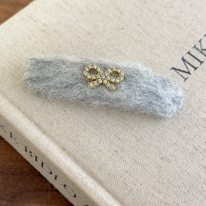 Close-up of grey felt hair clip featuring a gold metal bow with sparkling rhinestones