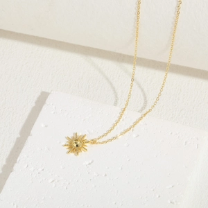 Macro detail of a 14K gold plated sunburst pendant on white textured stone tile