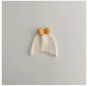 Detailed close-up of cream knit baby hat with vertical ribbed texture and yellow bows