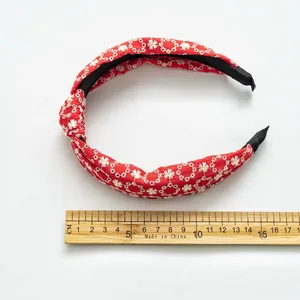 Red fabric knotted headband with white floral embroidery and 15cm measurement scale