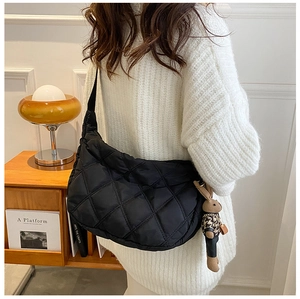 Close-up of black quilted hobo bag with a cute rabbit pendant worn over a white sweater