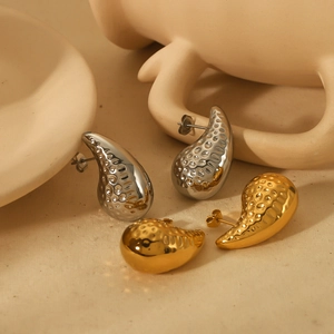 Exaggerated 18k gold and silver teardrop earrings with hammered texture on linen