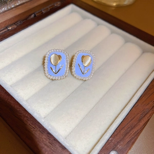 Close-up of light blue tulip earrings with cat-eye stone and white pearl borders