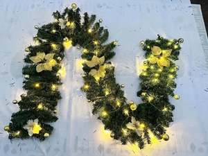 Detail of green PVC Christmas garland with gold ornaments and warm LED lights